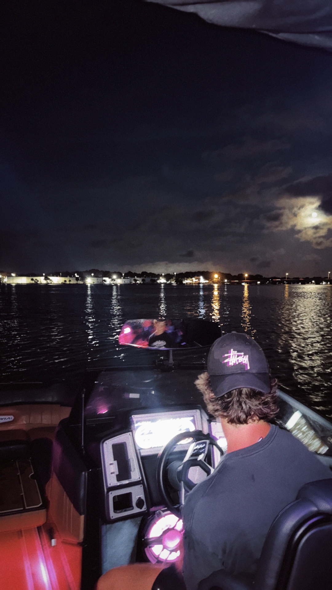 Driver at the helm of the Supra boat at night with pink deck lighting