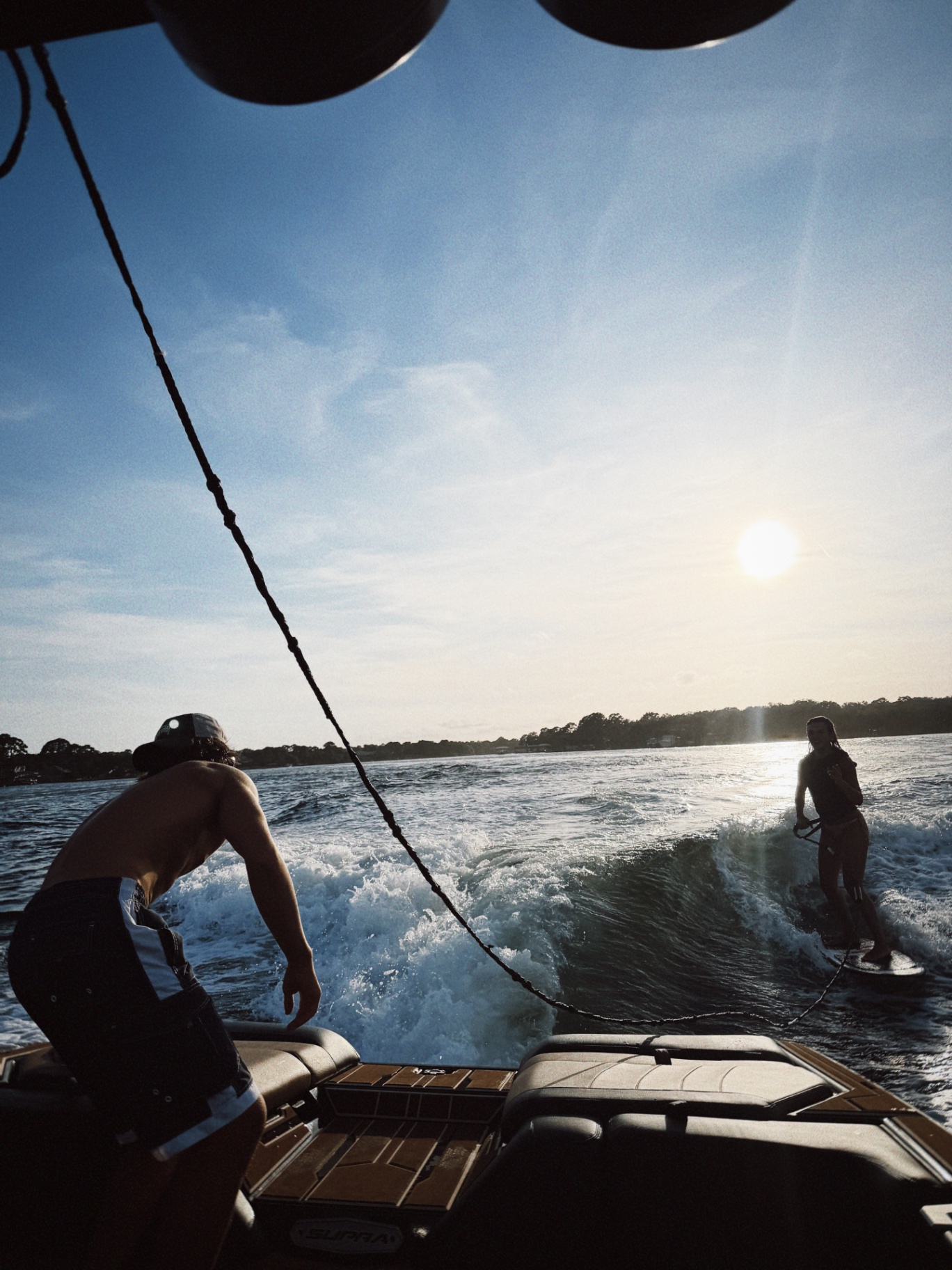 Wakesurfer riding behind the Supra boat in golden afternoon light